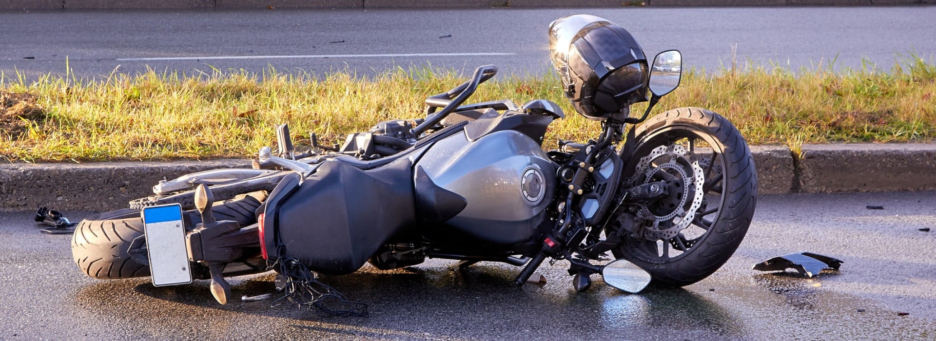 Motorcycle down on its side on the asphalt beside a helmet and scattered debris